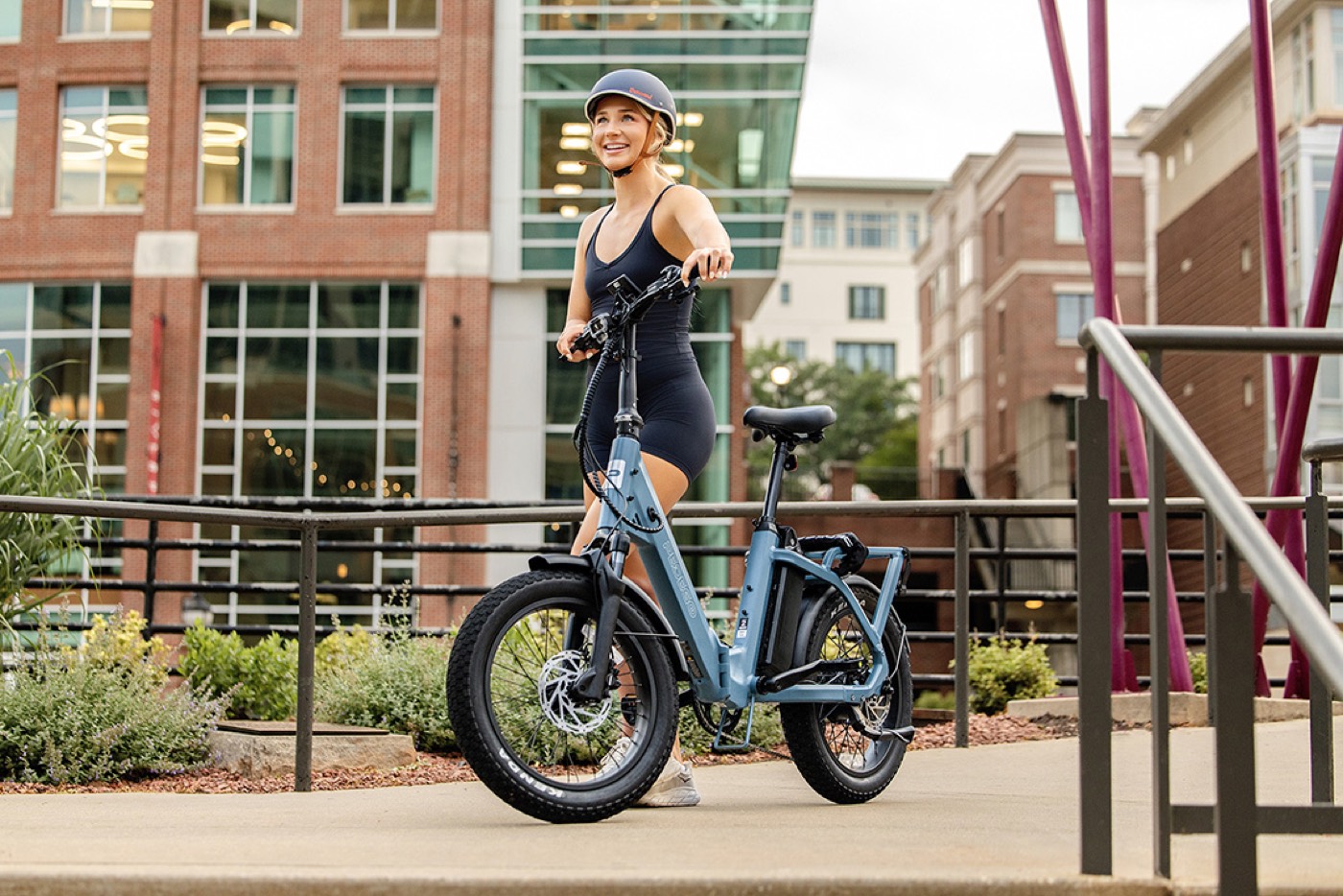 Someone standing with a blue Pedego Latch 2 folding e-bike on a city street