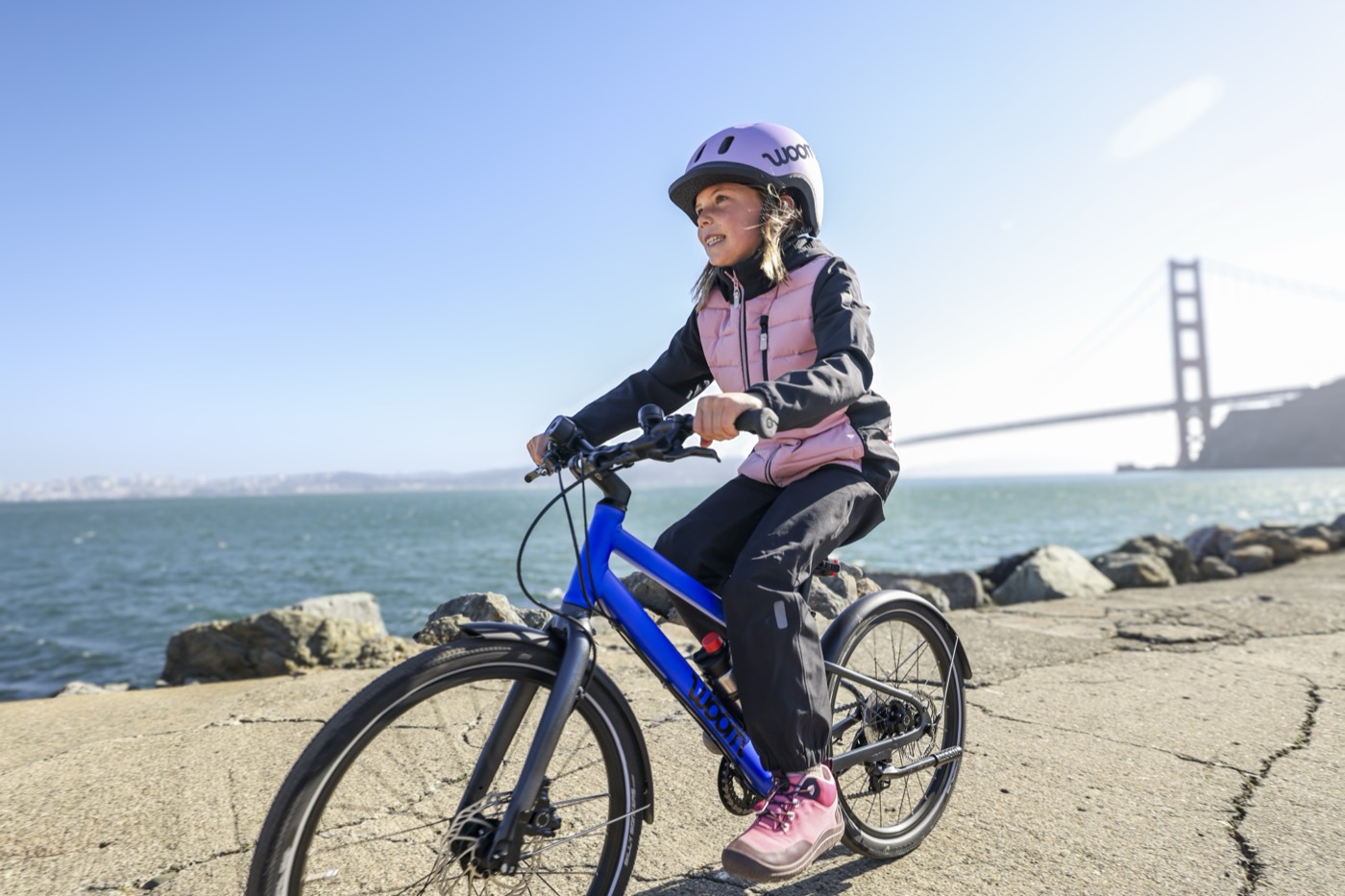 A child riding a blue Woom EXPLORE beside the water