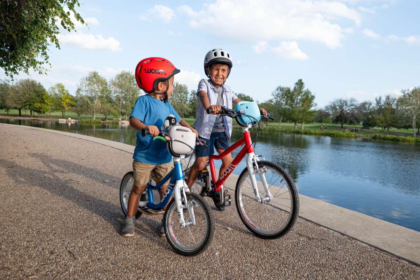 Two children riding Woom GO bikes on a path beside a lake