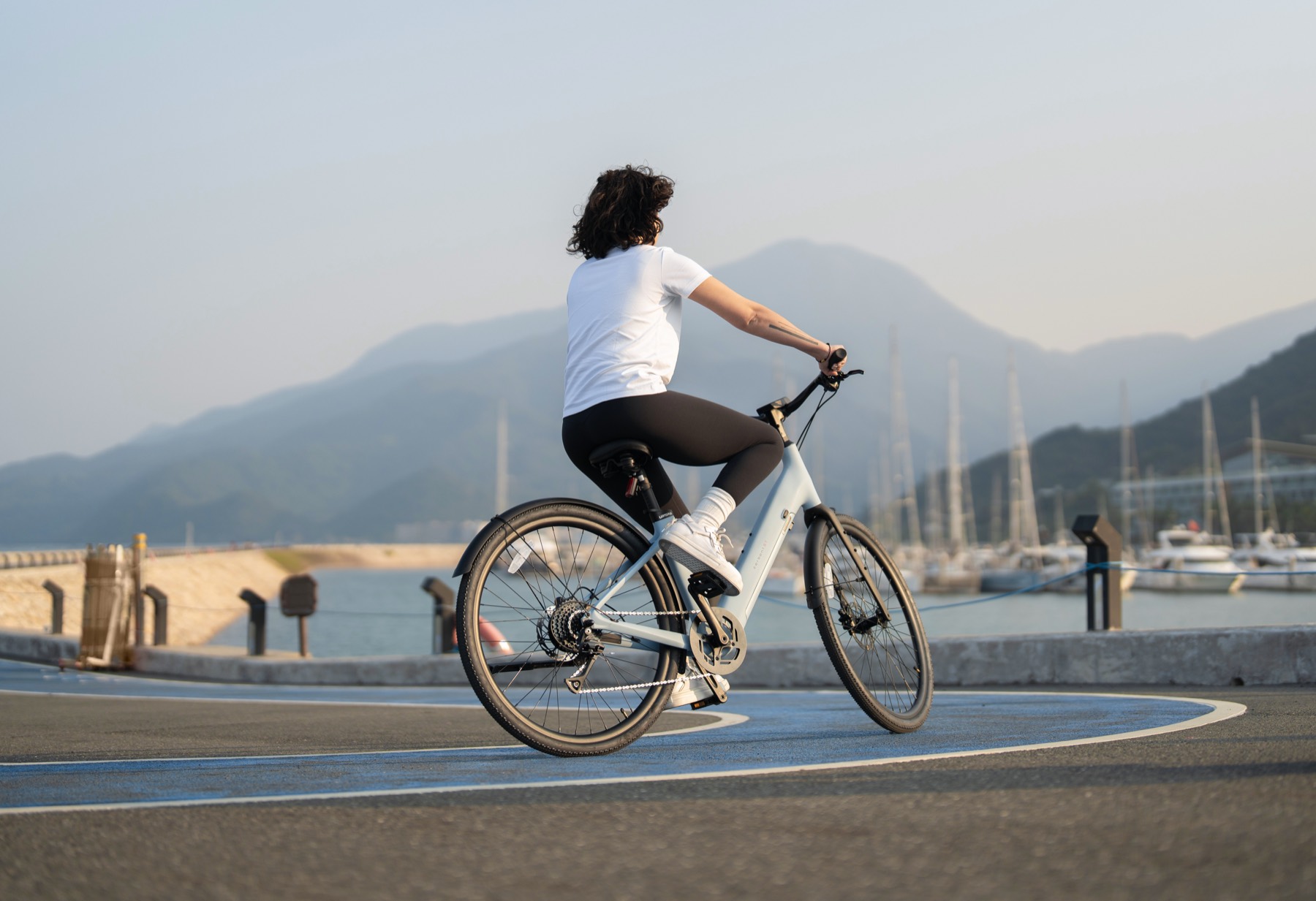 A rider on an Urtopia Carbon 1 ST on a waterfront path past moored boats