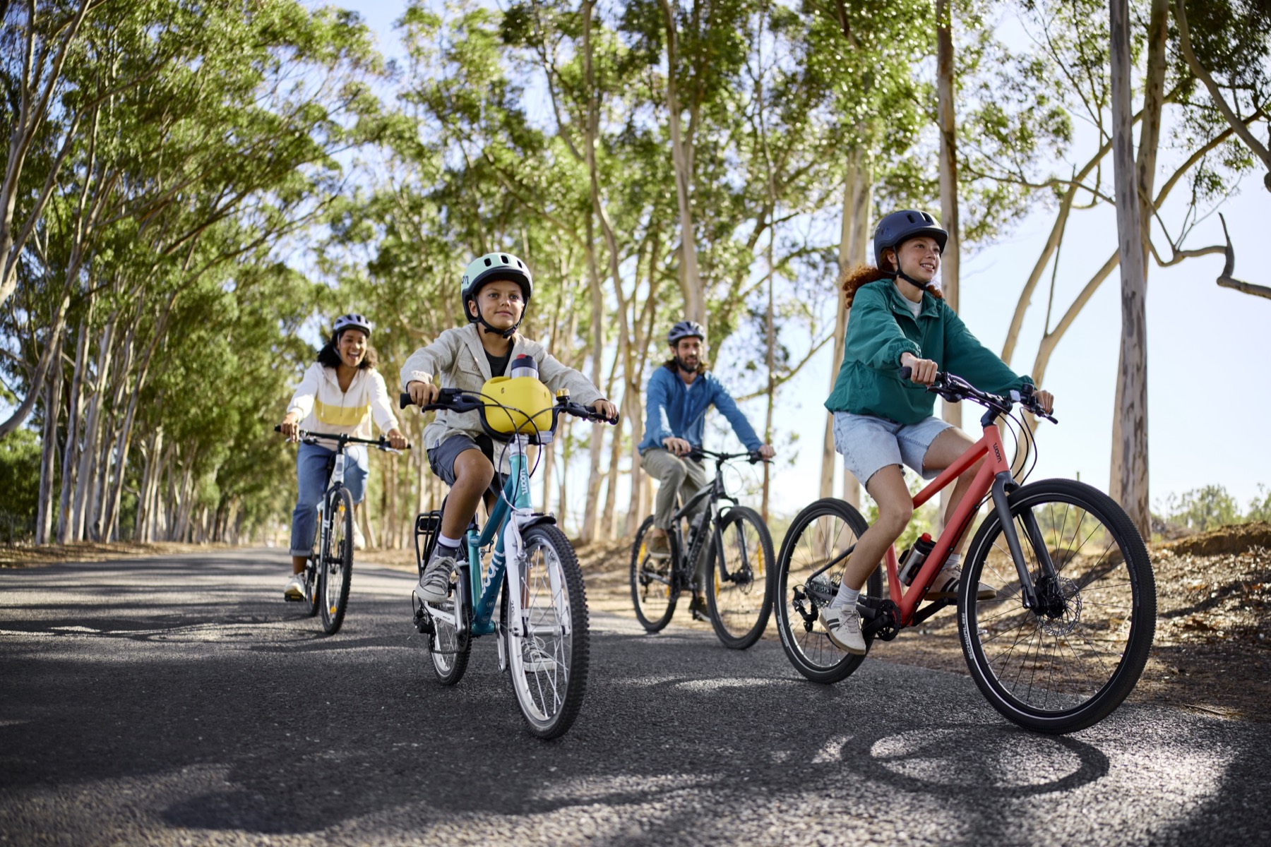 A family of four riding together on Woom bikes along a tree-lined road