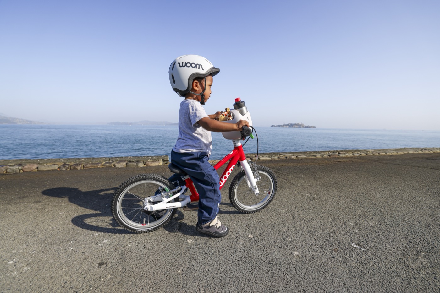 A young child riding a Woom bike on a path beside the water